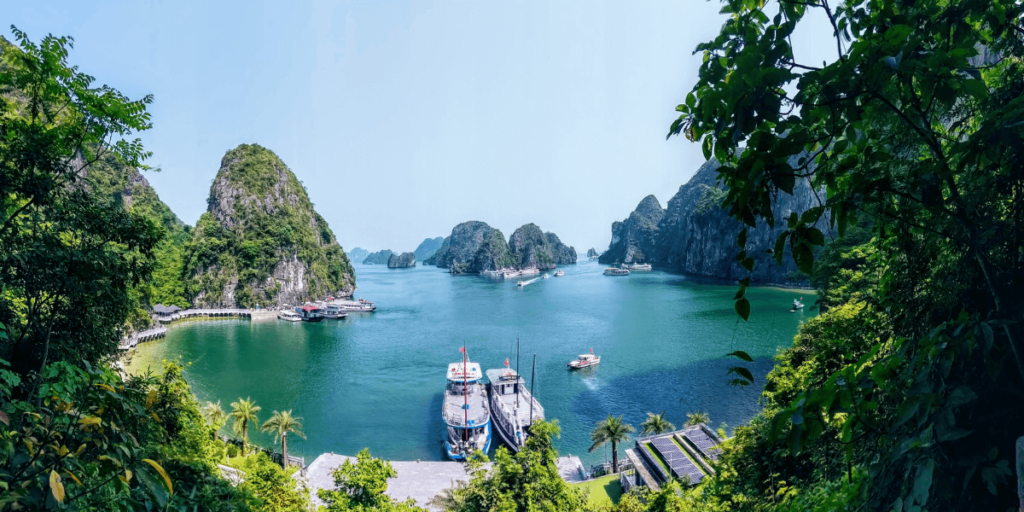 這張照片拍攝於越南北部著名的世界自然遺產 下龍灣(Hạ Long Bay)。畫面中可見碧綠的海水,點綴著數不清的石灰岩島嶼,形成獨特的喀斯特地形。岸邊停泊著遊船,這些船隻提供遊覽下龍灣的行程,帶旅客穿梭於壯麗的海蝕洞與奇岩之間。濃密的綠樹在畫面邊緣增添自然氛圍,使整體景色更顯寧靜與神秘。下龍灣是越南最受歡迎的旅遊景點之一,被譽為「海上桂林」,是來到越南北部不可錯過的絕美勝地。