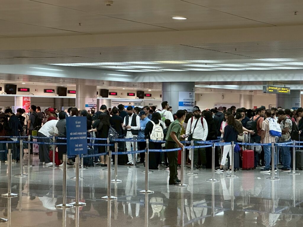 這張照片拍攝於越南機場入境大廳，可以看到大批旅客在入境查驗櫃檯前排隊等候，隊伍相當擁擠，場內人潮眾多，旅客帶著行李箱，現場秩序由圍欄及指示牌維持。畫面清楚展現旺季或高峰時段入境越南時，過海關排隊等待時間冗長的現象，非常適合用於說明越南機場入境動線、旅遊旺季排隊或電子簽證入境經驗的文章配圖。