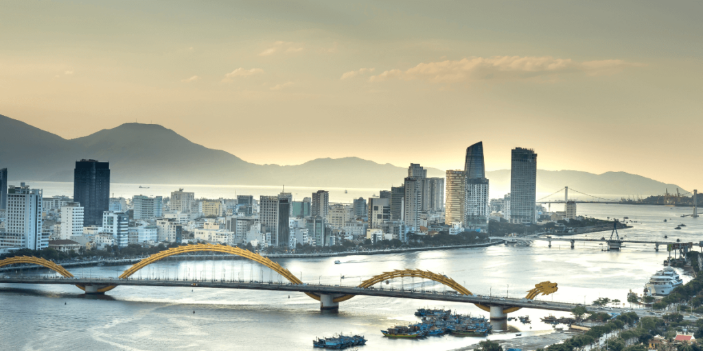 這張圖片展示了越南峴港的龍橋（Dragon Bridge），傍晚時分，橋的燈光和城市的天際線交織在一起。這座橋是峴港的標誌性建築，白天和夜晚的景象各具特色。大橋的造型像一條巨龍，象徵著越南的力量和文化。