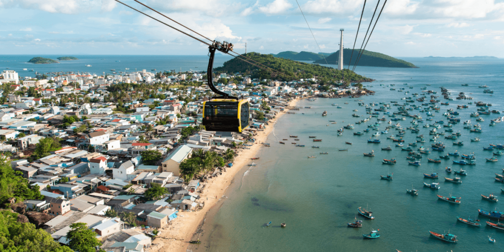 這張圖片展示了越南富國島(Phú Quốc)著名的纜車景觀。纜車從島嶼的一側穿越至另一側,空中俯瞰整個海岸線和漁船群。清澈的海水與島嶼的綠意交織,呈現出壯麗的自然景觀,讓人沉醉於這片熱帶天堂。